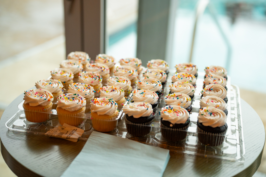 A tray of cupcakes under rainbow sprinkles, waiting by the window