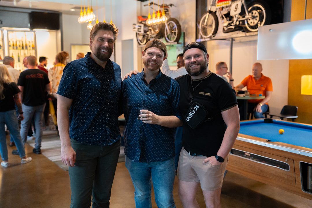 Three friends arm in arm by the pool table, all grinning