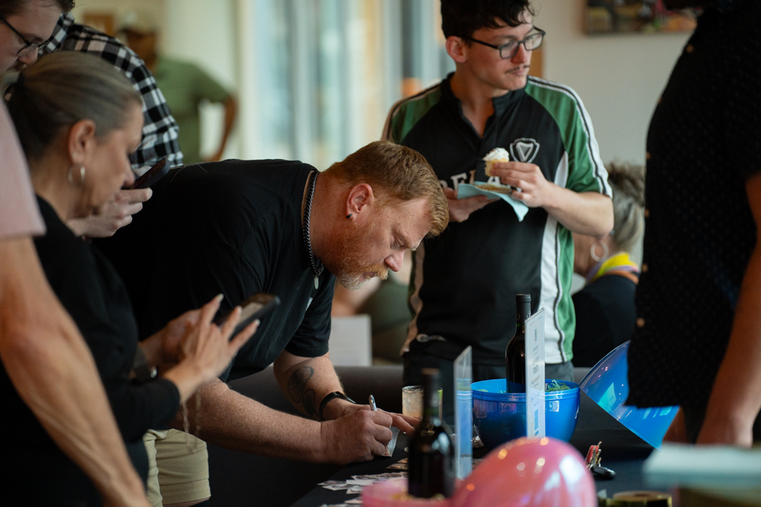 Filling out raffle tickets at the charity table, cupcake in hand behind him